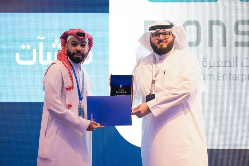 Ahmed Alshareef handing over a plaque on a Monsha'at stage